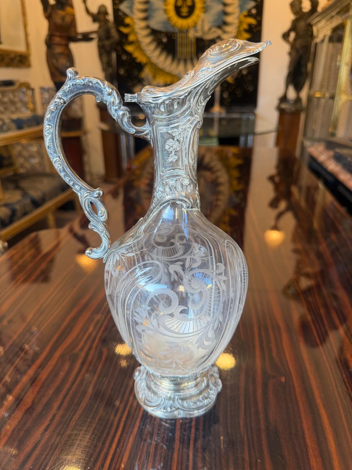 Carafe à vin en cristal gravé à monture d'argent de style rocaille, couvercle à charnière formant bec verseur et anse feuillagée, sur une table d'acajou
