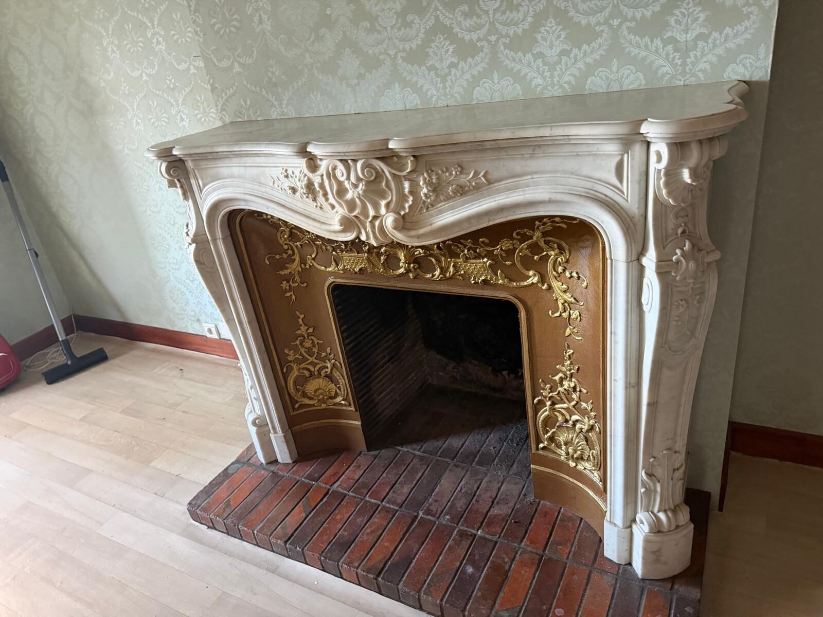 Cheminée de style Louis XV en marbre blanc sculpté, linteau à coquille rocaille, jambages à volutes et intérieur à décor doré