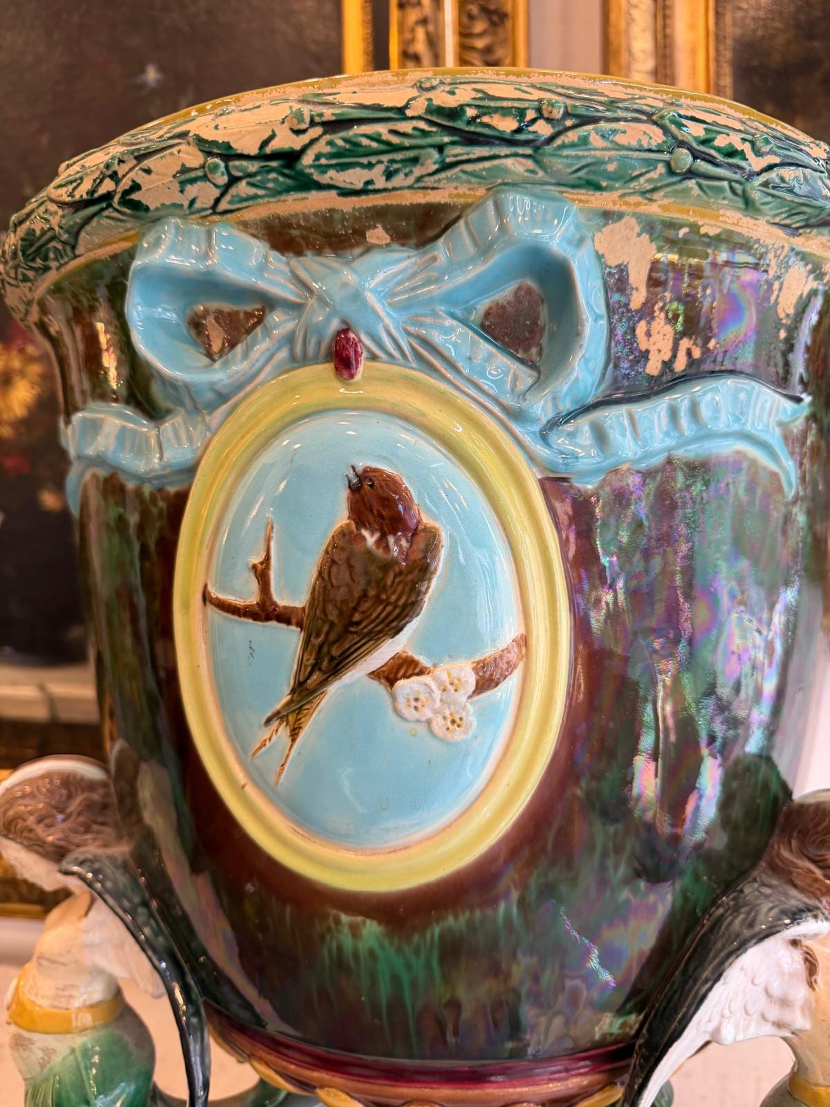 Médaillon ovale à fond turquoise : un oiseau en relief sur une branche fleurie, sous un nœud de ruban bleu