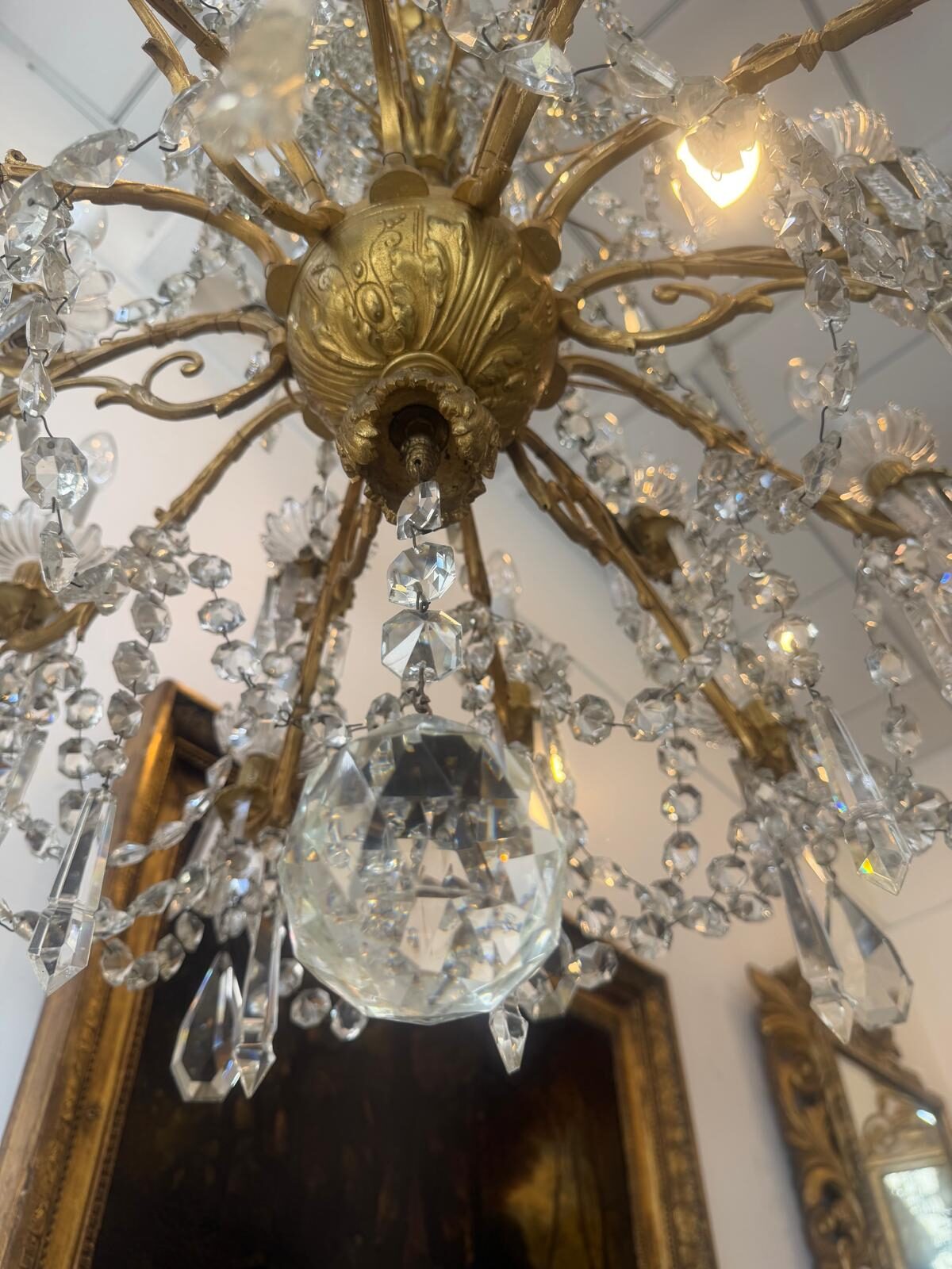 Dessous du lustre en contre-plongée : culot de bronze doré à godrons et grosse boule de cristal taillée à facettes