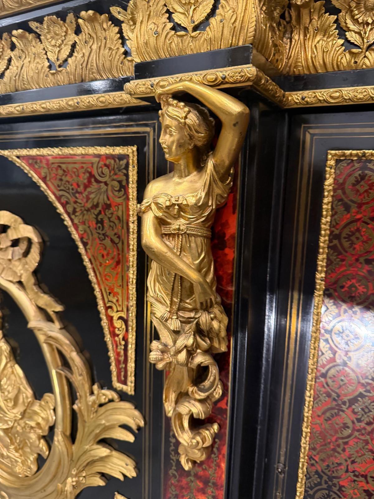 Détail d'une cariatide en bronze doré en applique sur un montant, à côté d'un panneau en marqueterie de laiton sur fond rouge