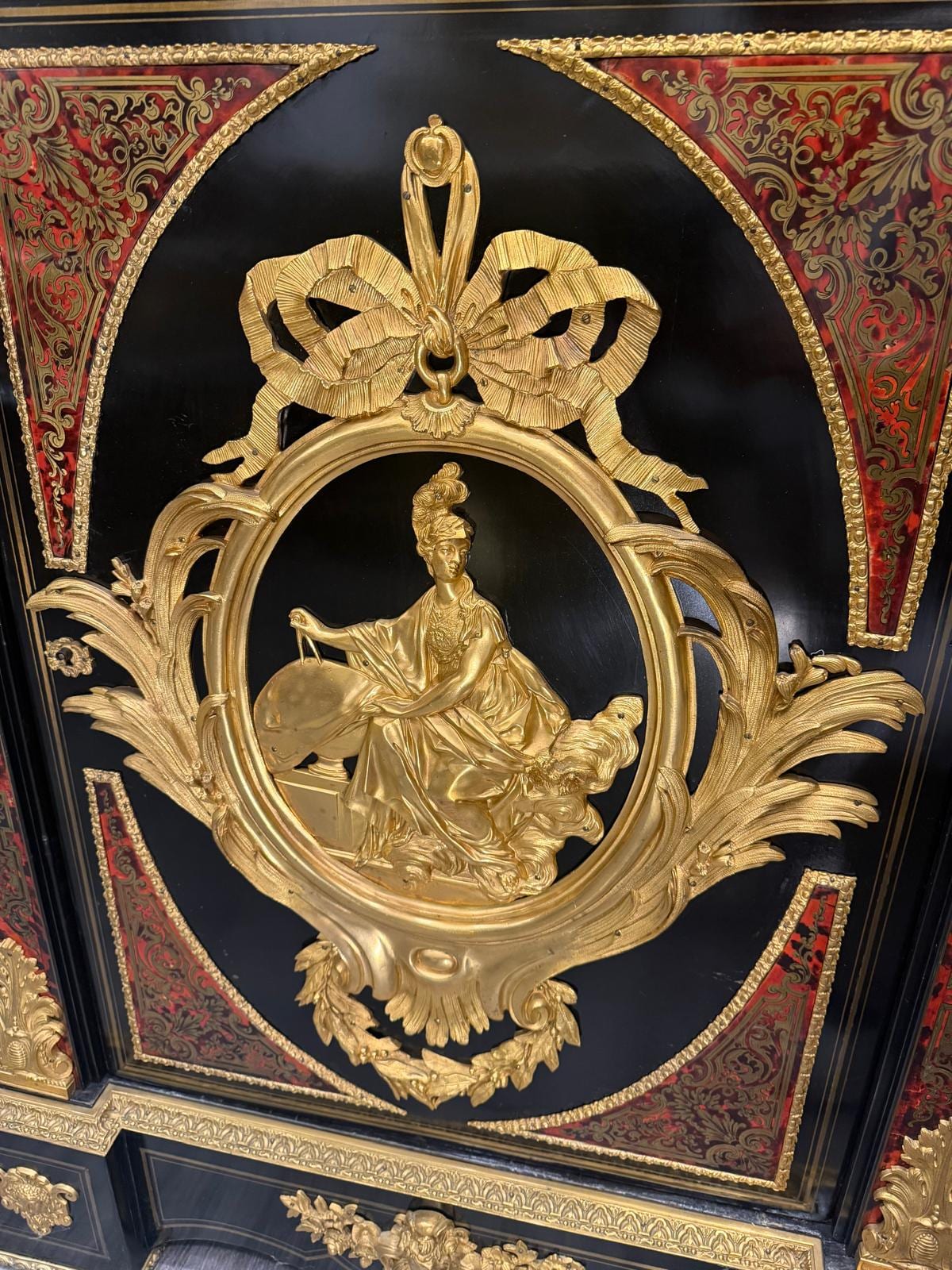 Détail du médaillon ovale en bronze doré : figure féminine casquée assise, encadrée de rinceaux et sommée d'un nœud de ruban