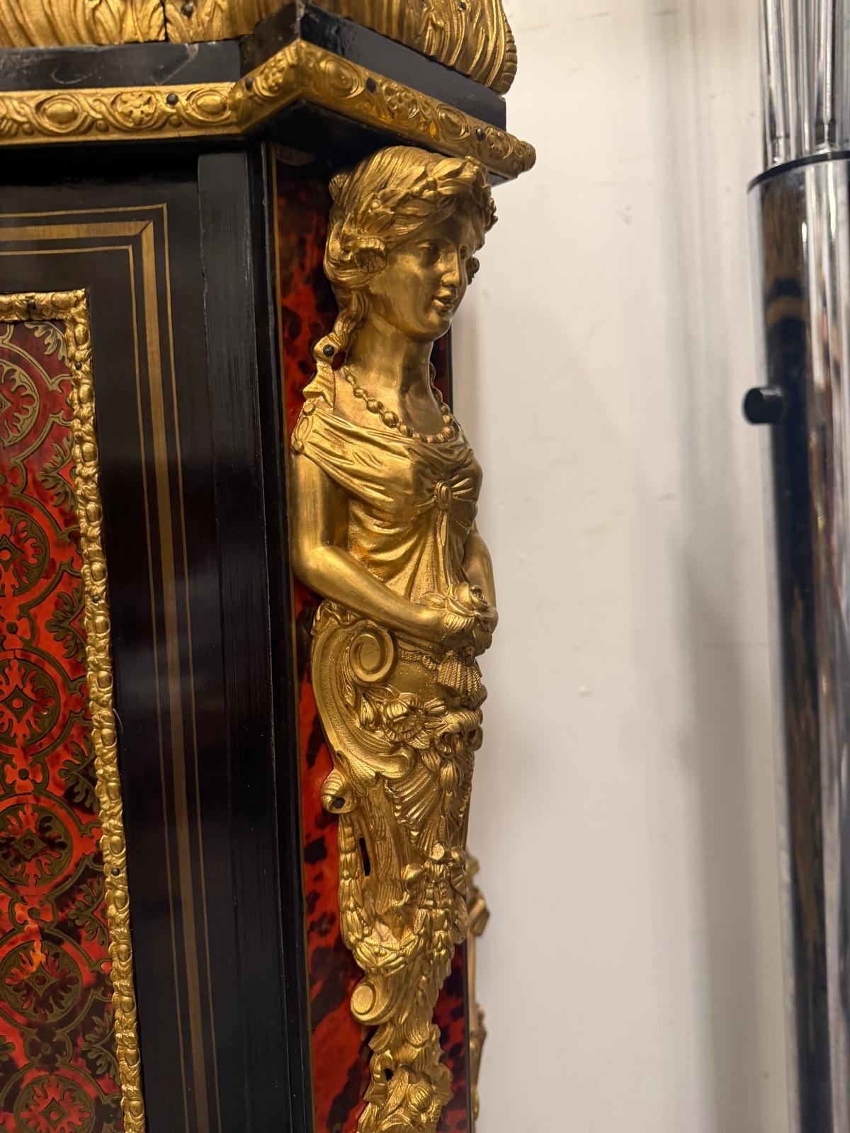 Une cariatide vue de profil, bras levé, en bronze doré sur le montant noirci