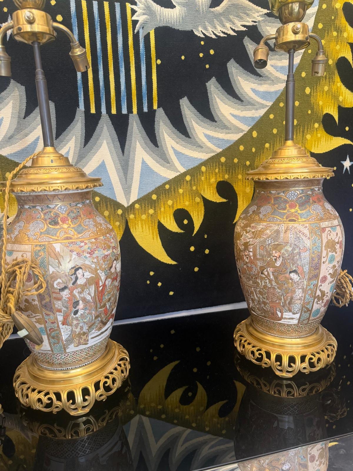 Paire de lampes montées sur des vases balustres en faïence de Satsuma, décor doré de personnages et de fleurs, bases en bronze doré ajouré, devant une tapisserie à motif de soleil