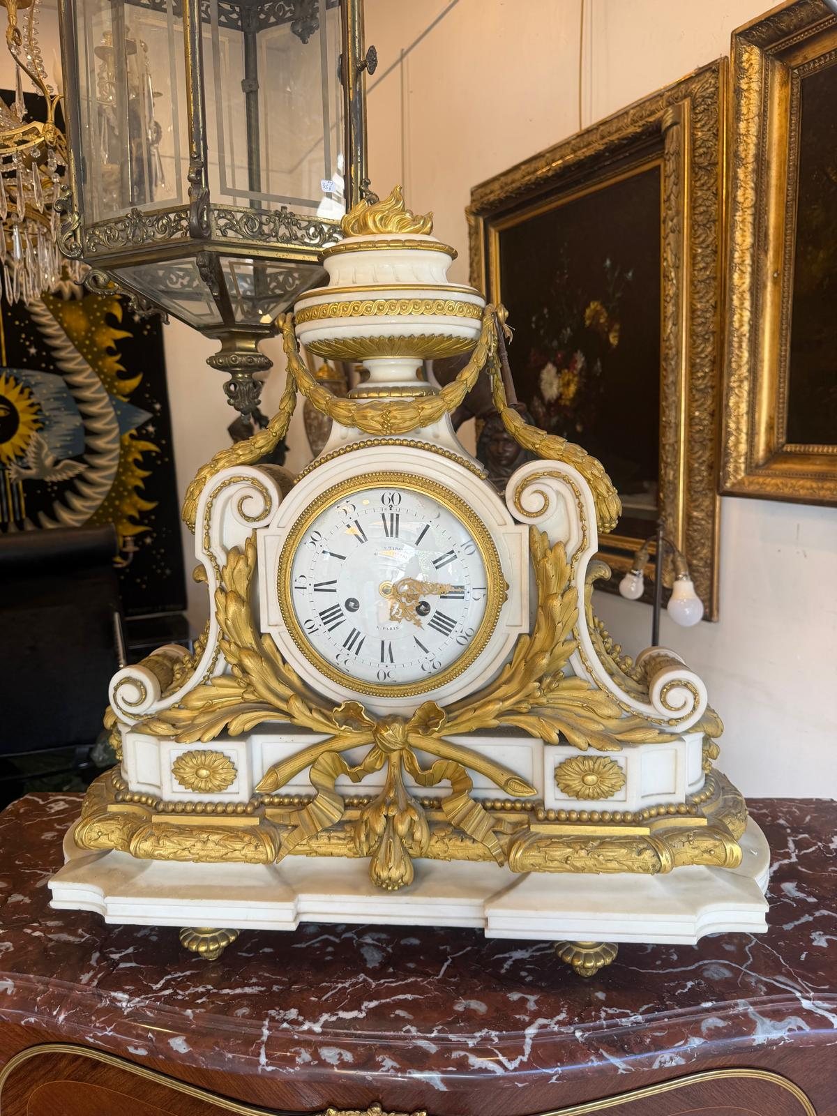 Pendule de cheminée de style Louis XVI en marbre blanc et bronze doré, surmontée d'un pot à feu, posée sur une console de marbre rouge