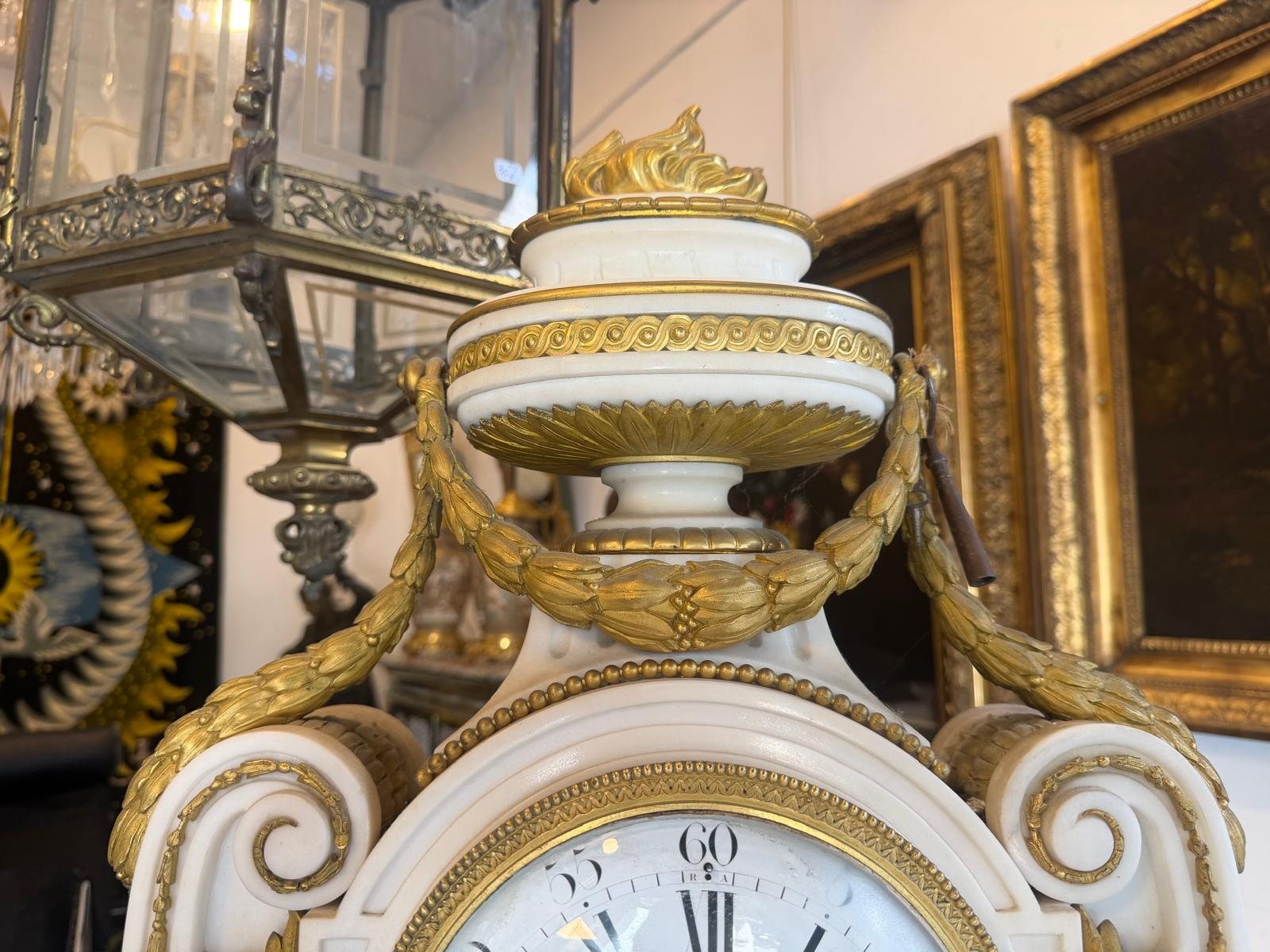 Pot à feu en marbre blanc et bronze doré au sommet de la pendule, flammes dorées et guirlandes de laurier