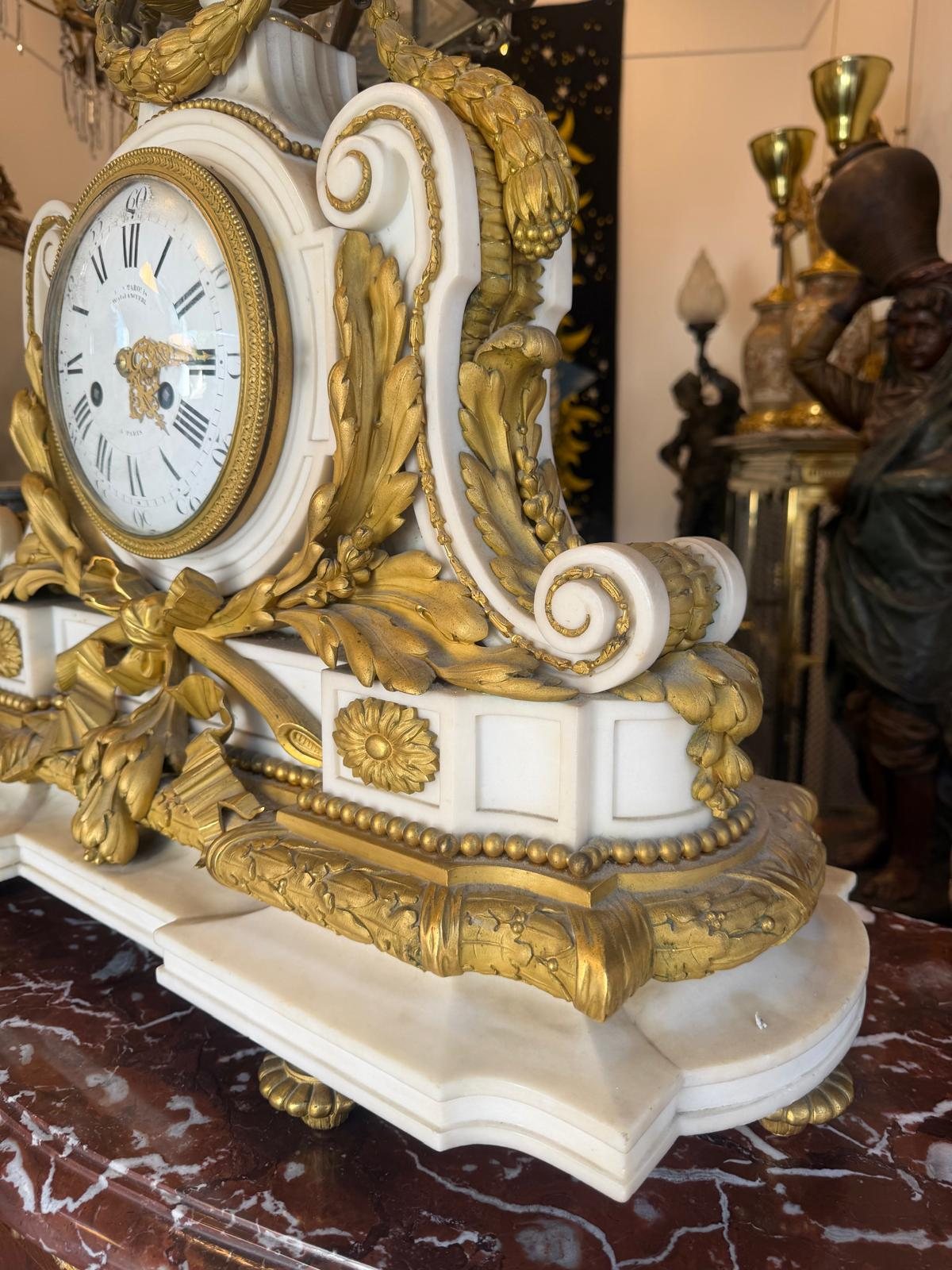 La pendule vue de profil : volute de marbre blanc, rosaces et feuillages en bronze doré, terrasse à rang de perles