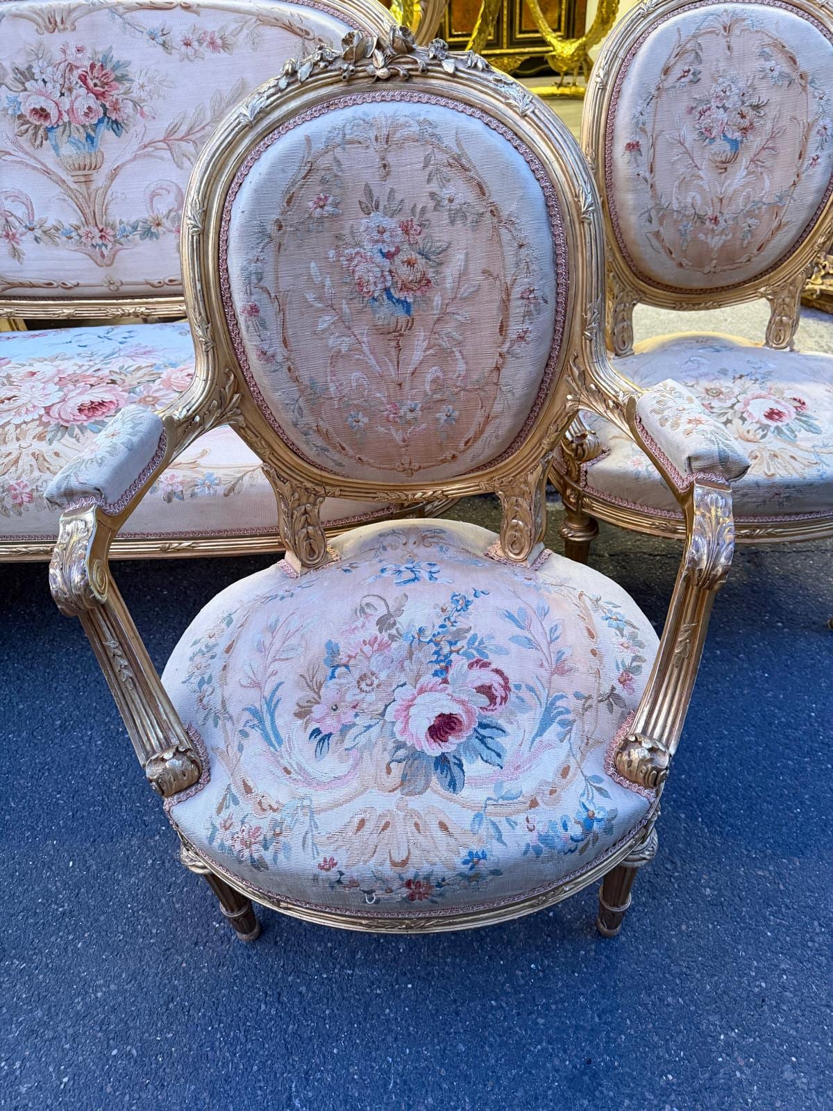 Fauteuil à dossier médaillon en bois sculpté et doré, sommé d'un nœud de ruban, garni de tapisserie à bouquets de roses sur fond clair