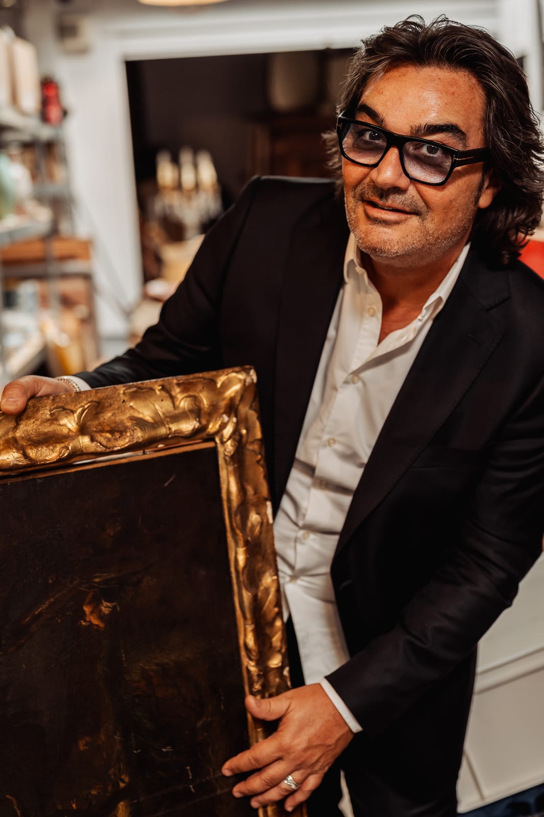 Éric BENHAMOU sourit en tenant le tableau dans son cadre doré, dans sa réserve