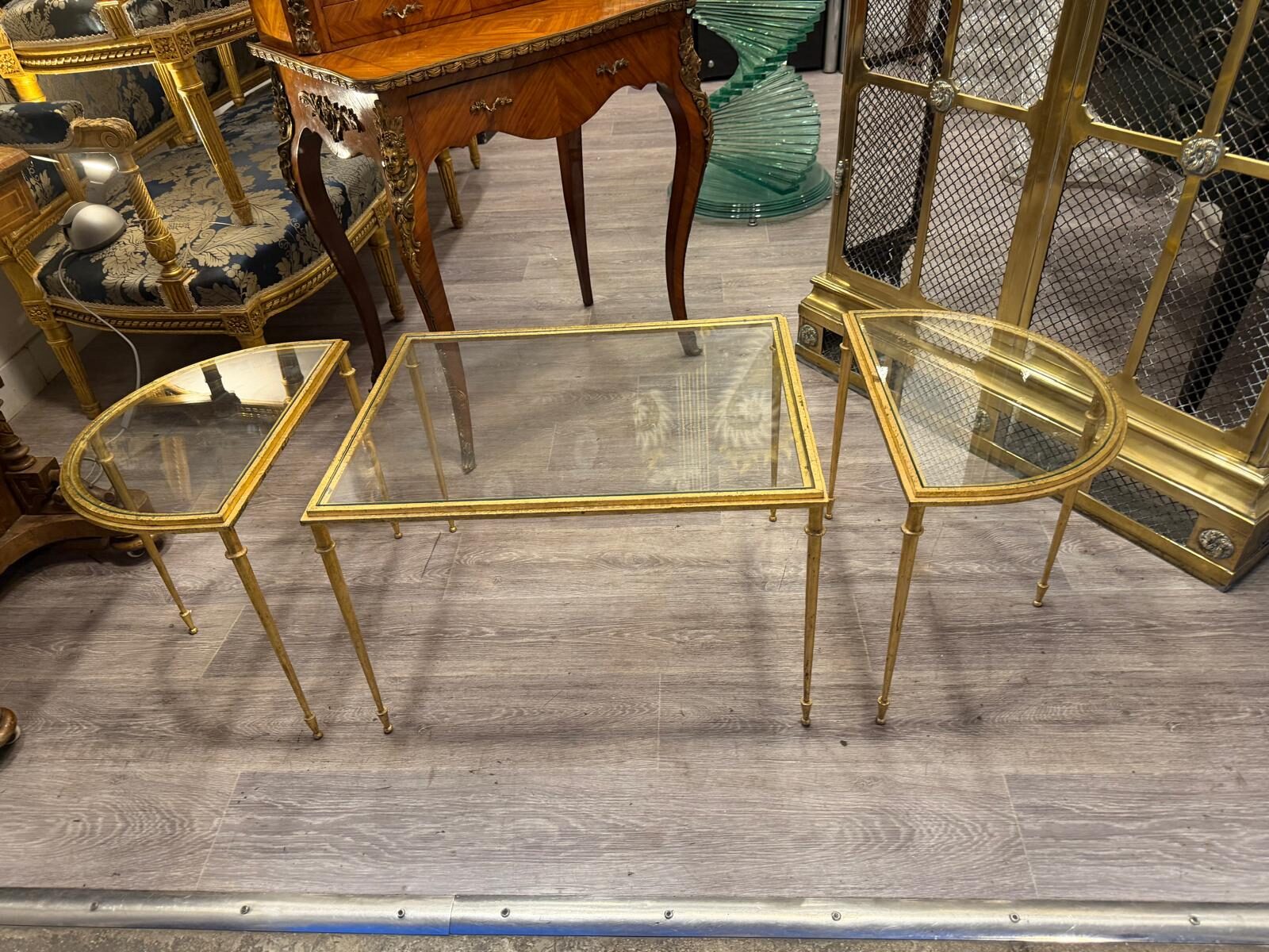 Les tables gigognes dorées dans une allée de la galerie, devant un bonheur du jour et un meuble en laiton grillagé