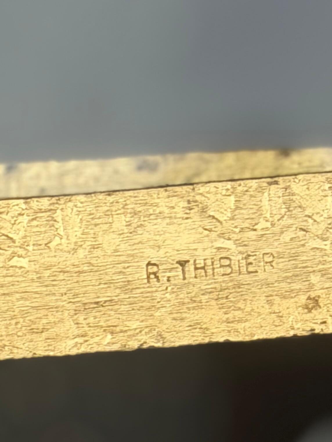 Gros plan sur la signature R. Thibier frappée dans la dorure à la feuille de la structure en fer forgé